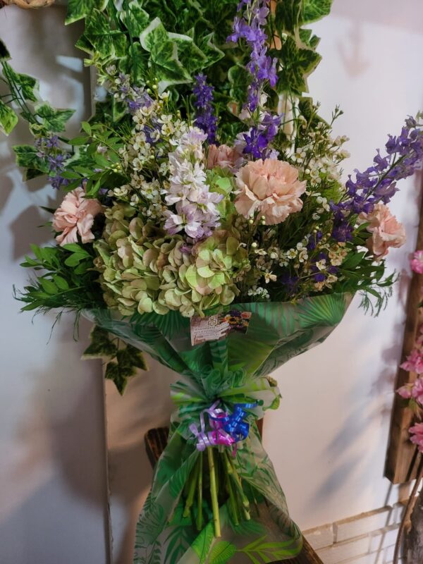 Ramo variado con hortensias, claveles y flores silvestres en tonos pastel, atado con un lazo decorativo, de Floristería Azahar 33.