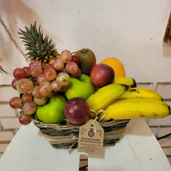Cesta artesanal llena de frutas frescas, incluyendo piña, mango, manzanas, uvas y plátanos, de Floristería Azahar 33.