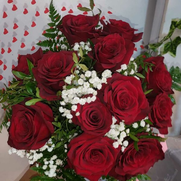Ramo de rosas rojas y gypsophila en papel de regalo con corazones, de Floristería Azahar 33, simbolizando amor y pasión.